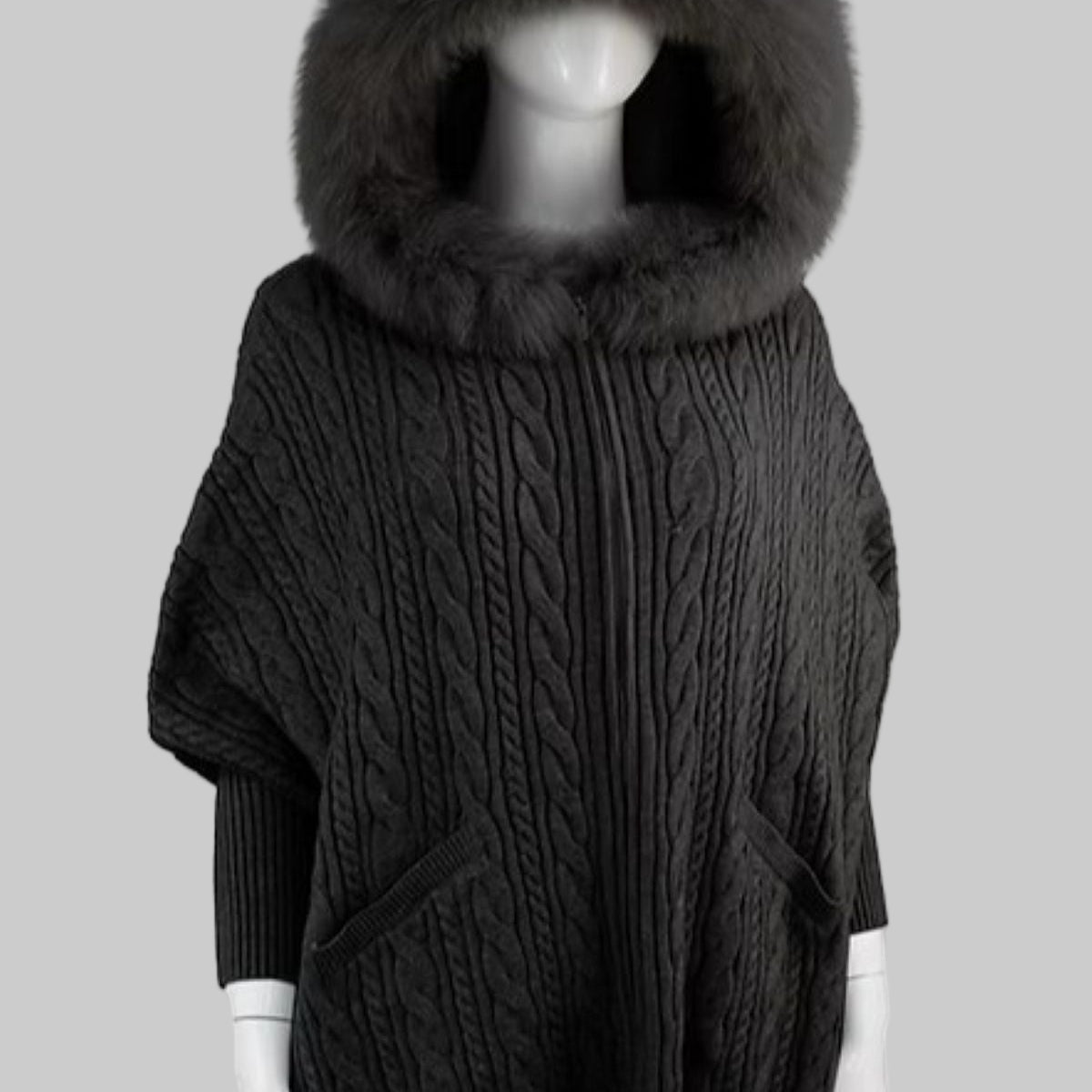 Dark gray cable knit poncho with a large fur hood on a mannequin against a white background