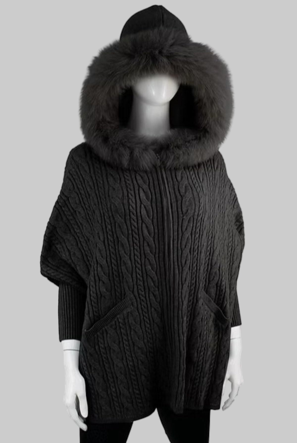 Dark gray cable knit poncho with a large fur hood on a mannequin against a white background